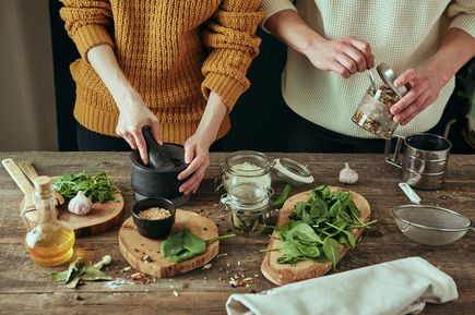 Zwei Personen bereiten frische Zutaten und Kräuter auf einem Holztisch zu