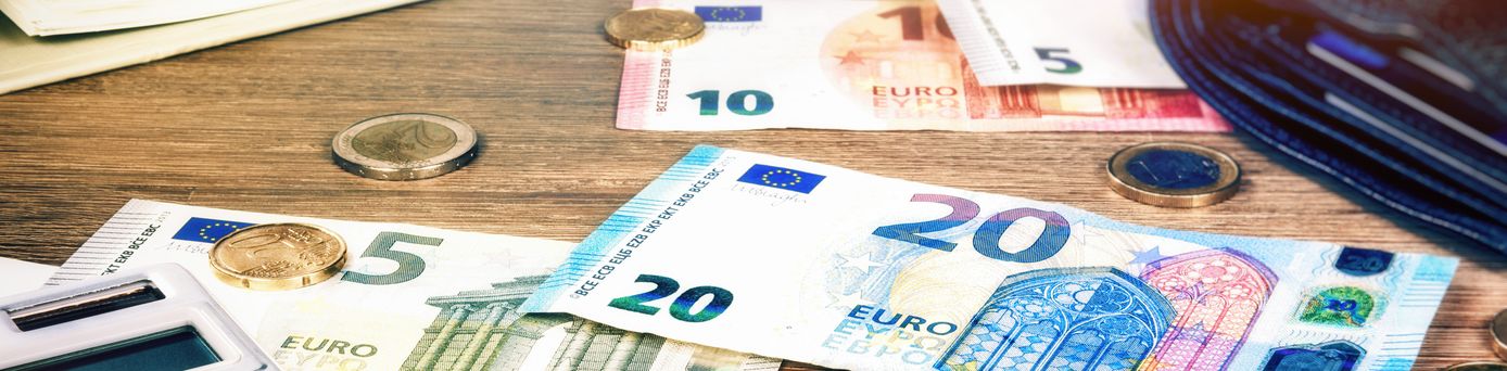 Verschiedene Euro-Banknoten und Münzen auf einem Holztisch neben einem Taschenrechner und einem Stift