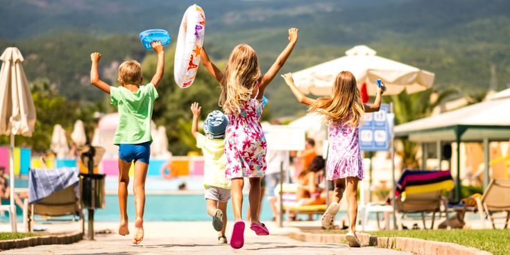 Vier Kinder laufen fröhlich mit Schwimmreifen zu einem Hotelpool in einer Ferienanlage