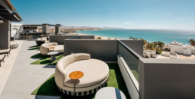 Terrasse mit runden Loungemöbeln und kleinen Tischen, Blick auf Meer und Küste, Teil des R2 Higos Beach Aparthotels.