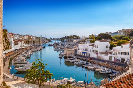 Der Hafen von Ciutadella auf Menorca ist von weißen Häusern, Restaurants und Booten gesäumt, die im ruhigen Wasser liegen