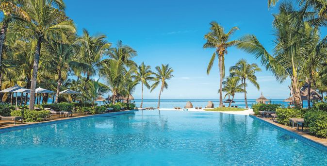 Großer Pool mit klarem Wasser umgeben von Palmen und Liegen mit Sonnenschirmen am Strand des Sugar Beach A Sunlife Resort Mauritius 