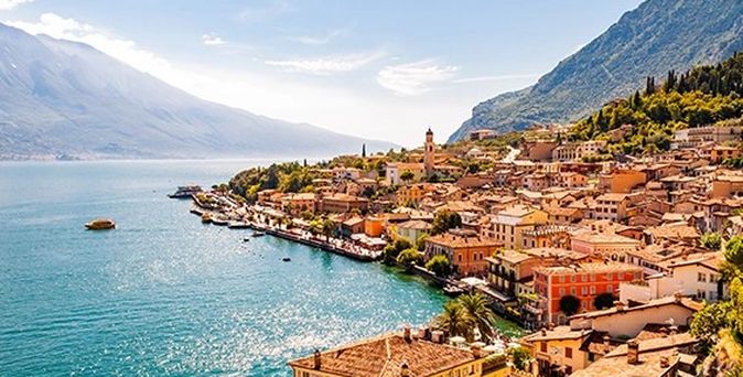 Küste mit felsigen Klippen und türkisfarbenem Meer in Albanien, im Hintergrund Berge und bewölkter Himmel