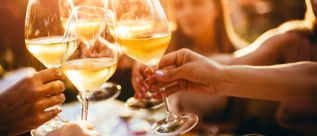 Mehrere Personen stoßen mit Gläsern Weißwein im warmen Abendlicht an