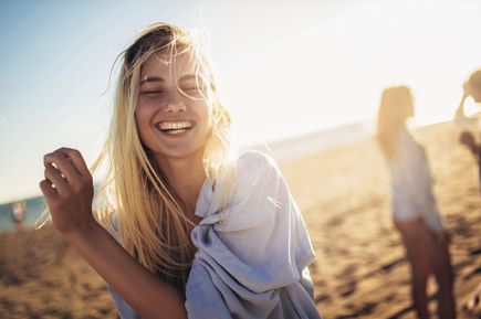 Person tanzt am Strand bei Sonnenuntergang mit wehenden Haaren im Gegenlicht