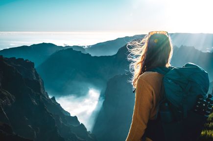 Person mit Rucksack blickt am Pico do Arieiro auf Madeira über eine Berglandschaft mit Wolken und tiefen Schluchten