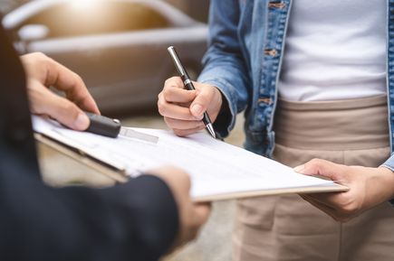 Person unterschreibt Formular auf Klemmbrett und erhält Autoschlüssel