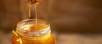 Honig, der von einem Löffel in ein Glas mit gelbem Band tropft