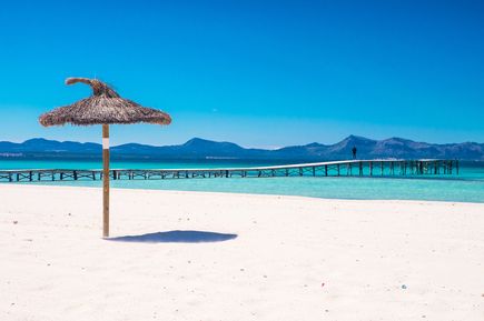 Weißer Sandstrand Playa de Muro auf Mallorca mit Holzsteg ins türkisfarbene Meer und Bergpanorama im Hintergrund