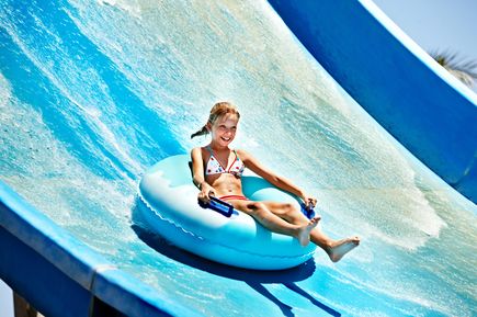 Mädchen rutscht lachend mit einem Schwimmreifen eine große blaue Wasserrutsche hinunter