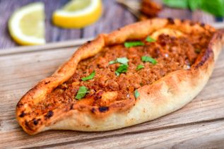 Türkische Pide mit würziger Hackfleischfüllung auf Holzbrett, garniert mit Petersilie und Zitronenscheiben