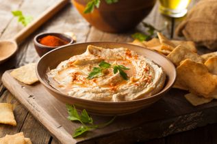 Cremiger Hummus in Schale mit Olivenöl und Paprika, serviert mit Pita-Chips auf Holzbrett