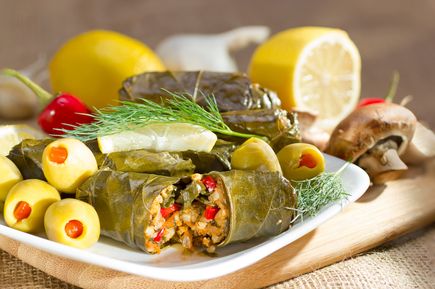 Gefüllte Weinblätter Dolma auf Teller, aufgeschnitten mit Reis-Gemüse-Füllung, dazu Zitronen und Kräuter