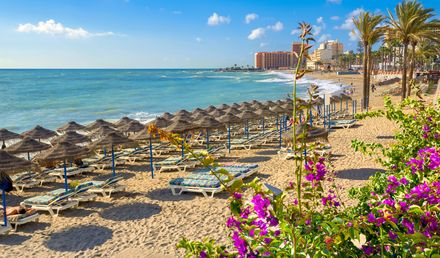 Strand von Benalmádena an der Costa del Sol mit Reihen von Sonnenschirmen und Liegen, Palmenpromenade sowie Hotels entlang der Mittelmeerküste