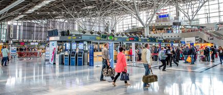 Innenansicht von Terminal 1 am Flughafen Stuttgart mit Check-in-Schaltern, digitalen Anzeigetafeln und Reisenden mit Gepäck in der lichtdurchfluteten Abfertigungshalle
