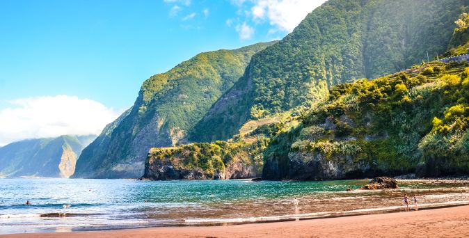 Klippen mit üppiger Vegetation über ruhigem Meer an der Küste von Madeira unter blauem Himmel