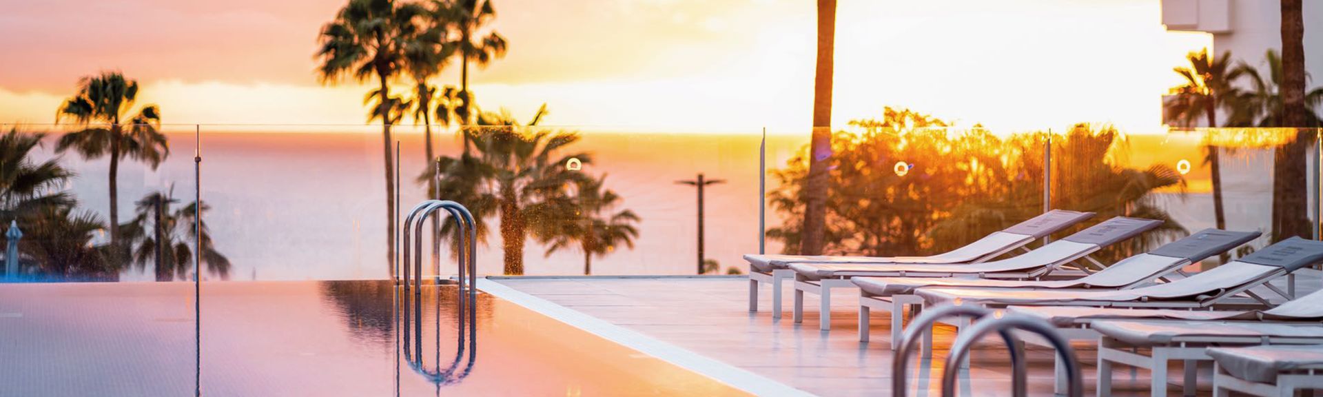Infinity-Pool mit Liegestühlen und Palmen im Sonnenuntergang