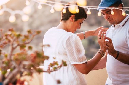 Paar tanzt im Freien bei Sonnenuntergang, Frau trägt weiße Bluse mit Puffärmeln, Mann trägt weißes Poloshirt.