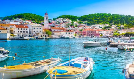 Hafenansicht von Pučišća auf der Insel Brač in Kroatien mit kleinen Booten im klaren Wasser, historischen Gebäuden und grünen Hügeln