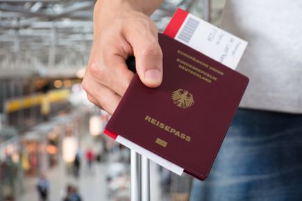 Hand hält einen deutschen Reisepass mit sichtbarem Flugticket in einem belebten Flughafen.