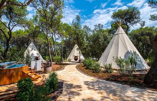 Tipi‑förmige Glamping‑Zelte des Arena One 99 Glamping Hotels inmitten eines grünen Pinienwaldes, verbunden durch einen Natursteinweg