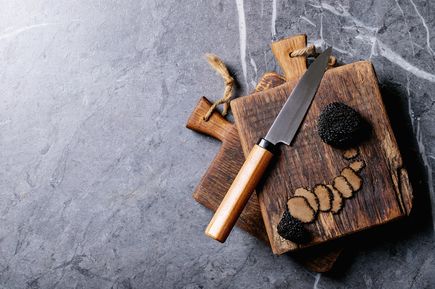 Frischer schwarzer Trüffel auf rustikalem Holzbrett mit Messer und Trüffelscheiben, hochwertige Feinkost-Zutat für Gourmetküche und mediterrane Gerichte