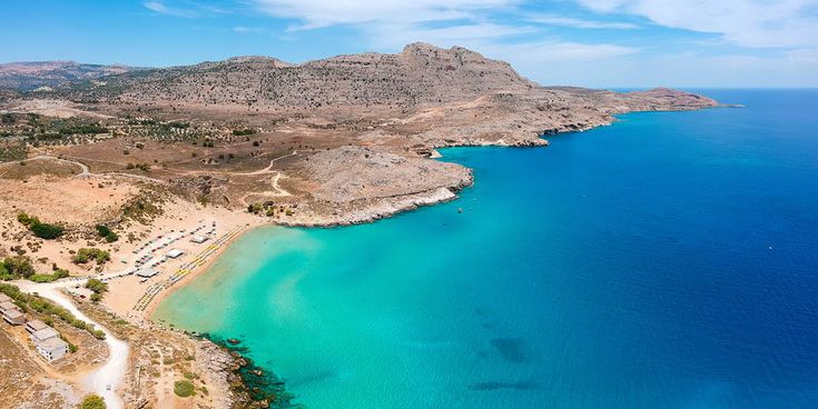 Küstenlandschaft von Rhodos mit klarem türkisfarbenem Wasser, felsigen Hügeln und einem kleinen Strand mit Sonnenschirmen