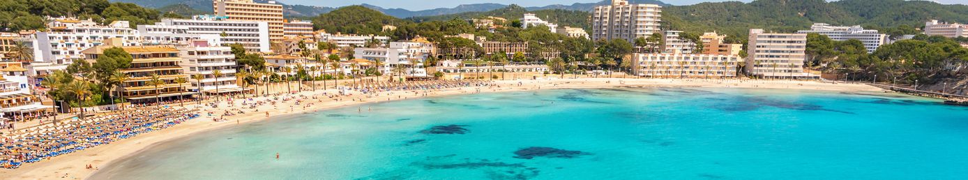 Panorama vom Strand von Paguera auf Mallorca mit klarem türkisfarbenem Wasser, Hotelanlagen und grünen Hügeln im Hintergrund