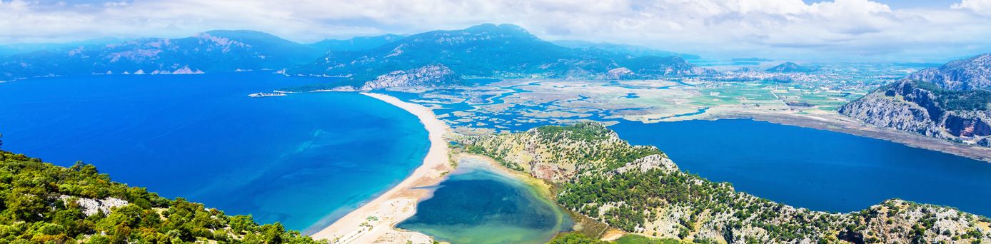 Panoramablick auf den Iztuzu Beach mit schmaler Landzunge zwischen Meer und Lagune, umgeben von grüner Hügellandschaft