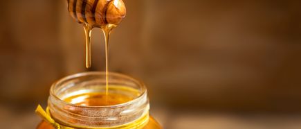 Honig, der von einem Holzlöffel in ein Glas mit gelbem Band tropft.