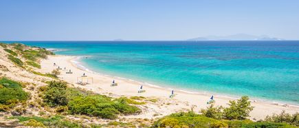 Langer Sandstrand mit vereinzelten Sonnenschirmen und türkisfarbenem Meer an der Küste von Kos