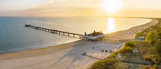 Luftaufnahme der historischen Seebrücke Ahlbeck auf Usedom mit breitem Sandstrand, Strandkörben und Ostseeküste bei Sonnenuntergang