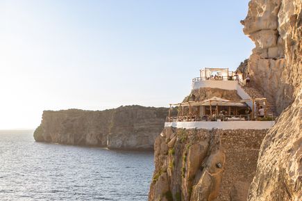 Cova d’en Xoroi Bar auf den Klippen von Menorca mit Terrassen und Blick über das Meer bei Sonnenuntergang