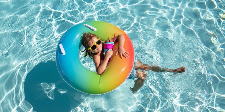Kind entspannt im bunten Schwimmreifen im Pool und hält ein Getränk in der Hand