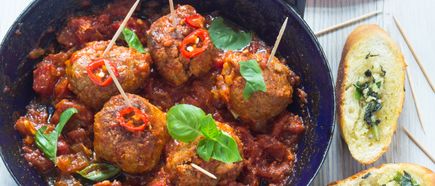 Fleischbällchen mit Basilikum und Chiliringeln auf Spießen in Tomatensauce neben Knoblauchbrot