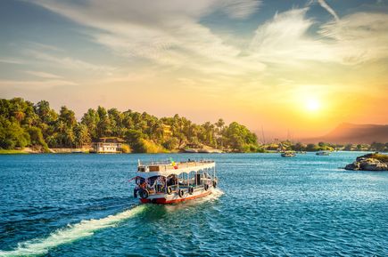 Touristenboot auf dem Nil in Ägypten bei Sonnenuntergang, umgeben von üppigen Palmen und grüner Landschaft, mit goldenem Himmel und ruhigem Wasser