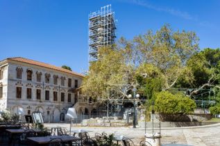 Historisches Gebäude mit Gerüst an einem Turm und Bäumen im Innenhof bei klarem Himmel