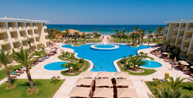 Große Poollandschaft des Royal Thalassa Monastir mit Palmen, Liegebereichen und direktem Blick auf den Sandstrand und das Meer.