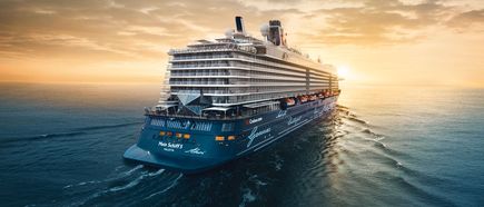 Das Kreuzfahrtschiff Mein Schiff 5 fährt bei Sonnenuntergang über das Meer und ist aus der Rückansicht zu sehen.