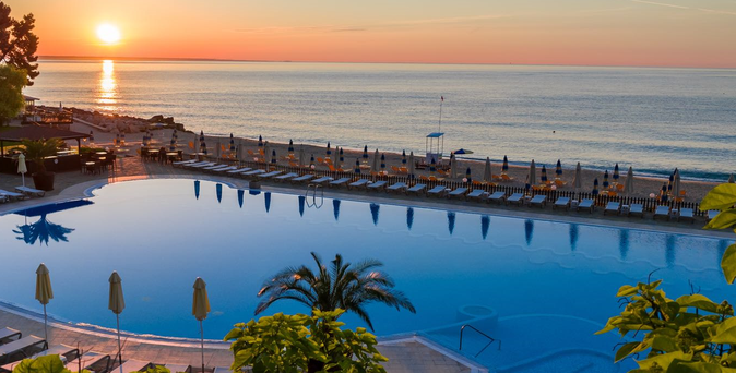 Sonnenuntergang über einem Pool mit Palmen, Liegen und Sonnenschirmen am Strand