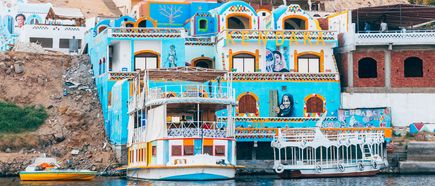 Farbige Häuser eines nubischen Dorfes am Ufer mit bemalten Fassaden und Booten auf dem Nil