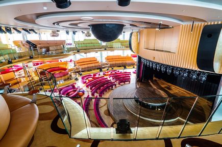 Das Theatrium der AIDAprima mit halbrunden Sitzreihen in kräftigen Farben, einer zentralen Bühne und modernen Beleuchtungsanlagen in einem offenen, mehrstöckigen Raum