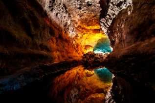 Höhleninnenraum der Cueva de Los Verdes auf Lanzarote mit unregelmäßigen Felswänden und einer Wasserfläche, die das farbige Licht reflektiert
