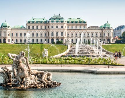 Barockschloss Belvedere mit grünen Kuppeln, davor Springbrunnen mit Skulpturengruppe in einem Wasserbecken, umgeben von Rasen und Wegen