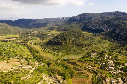 Luftaufnahme von Puigpunyent auf Mallorca mit grünen Feldern, Terrassenlandschaften, Wäldern und Bergen im Hintergrund