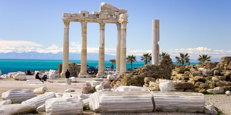 Antiker Apollon-Tempel in Side mit hohen Säulen direkt am türkisblauen Meer und Besuchern zwischen den historischen Ruinen