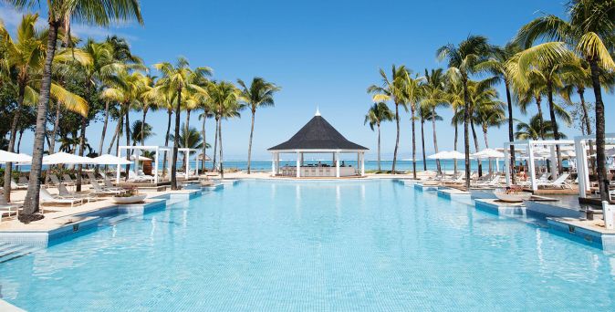 Großer Pool mit Palmen und Liegen an beiden Seiten sowie Pavillon am Ende mit Blick auf das Meer im Heritage Le Telfair Golf & Wellness Resort auf Mauritius