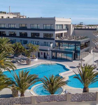 Moderner Hotelkomplex mit mehreren Stockwerken, Außenpool mit geschwungener Form, Palmen und Sonnenschirmen auf der Terrasse.