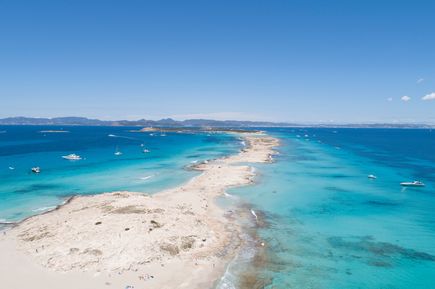 Luftaufnahme des Playa de Ses Illetes auf Formentera mit schmalem Sandstreifen, türkisblauem Meer und Booten im Wasser