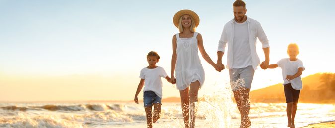 Familie mit zwei Kindern läuft am Strand bei Sonnenuntergang, alle tragen helle Kleidung